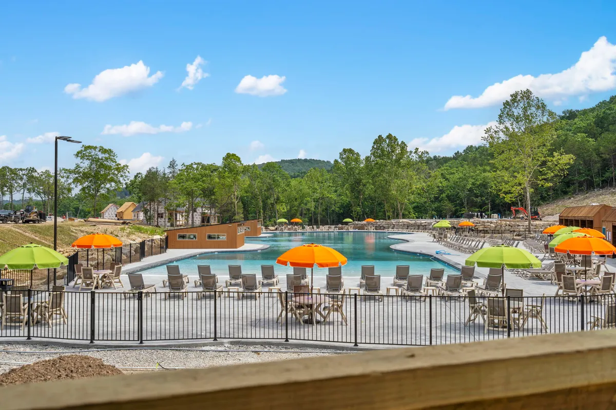 The image displays a vibrant outdoor swimming pool surrounded by colorful umbrellas, deck chairs, and lush trees. The pool area exudes a cheerful and welcoming atmosphere, perfect for family gatherings and summer fun.