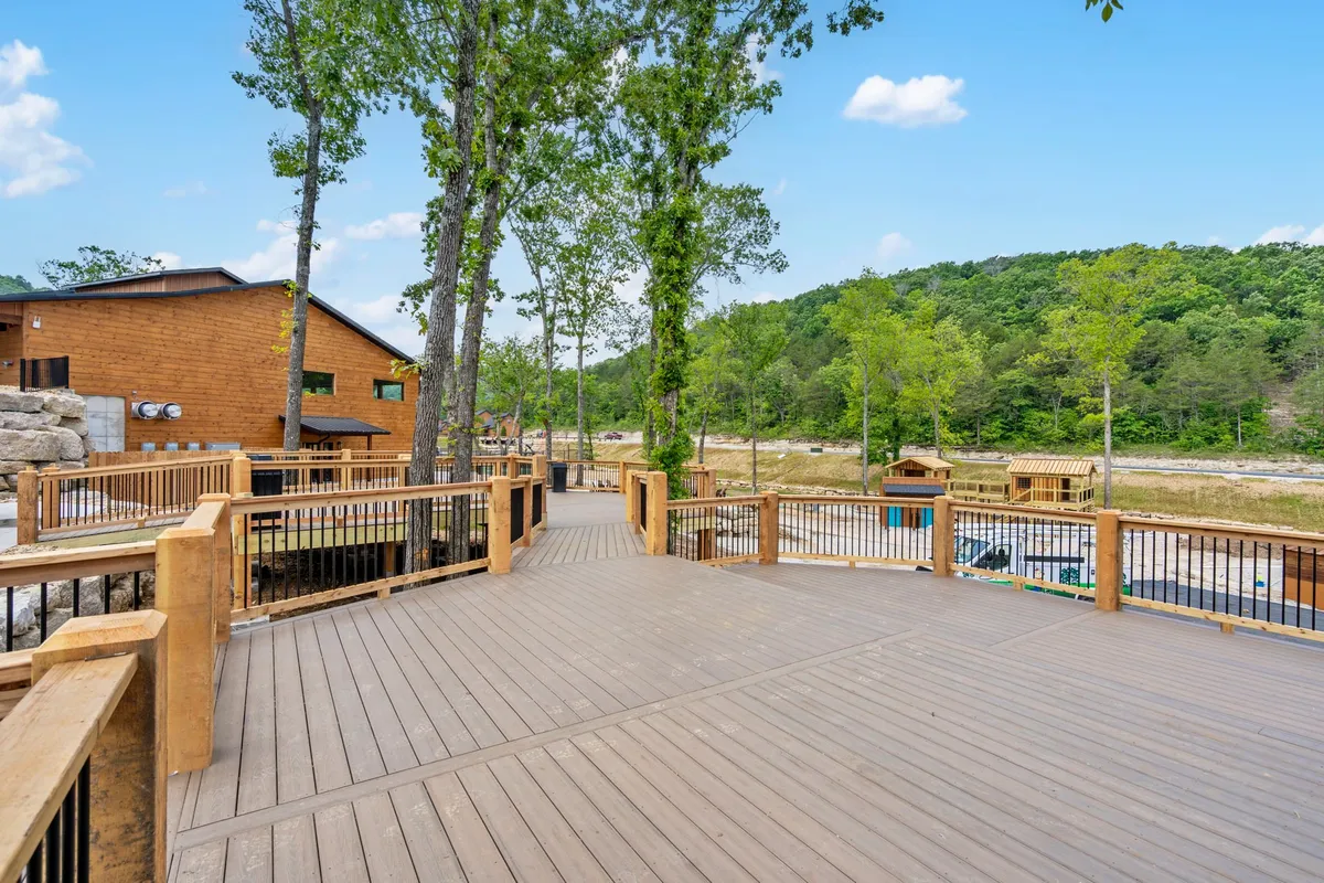 This image features a spacious wooden deck overlooking the treetops, distant hills, and nearby cabins. The tranquil setting is perfect for enjoying sunsets or relaxing outdoors with a pet by your side.