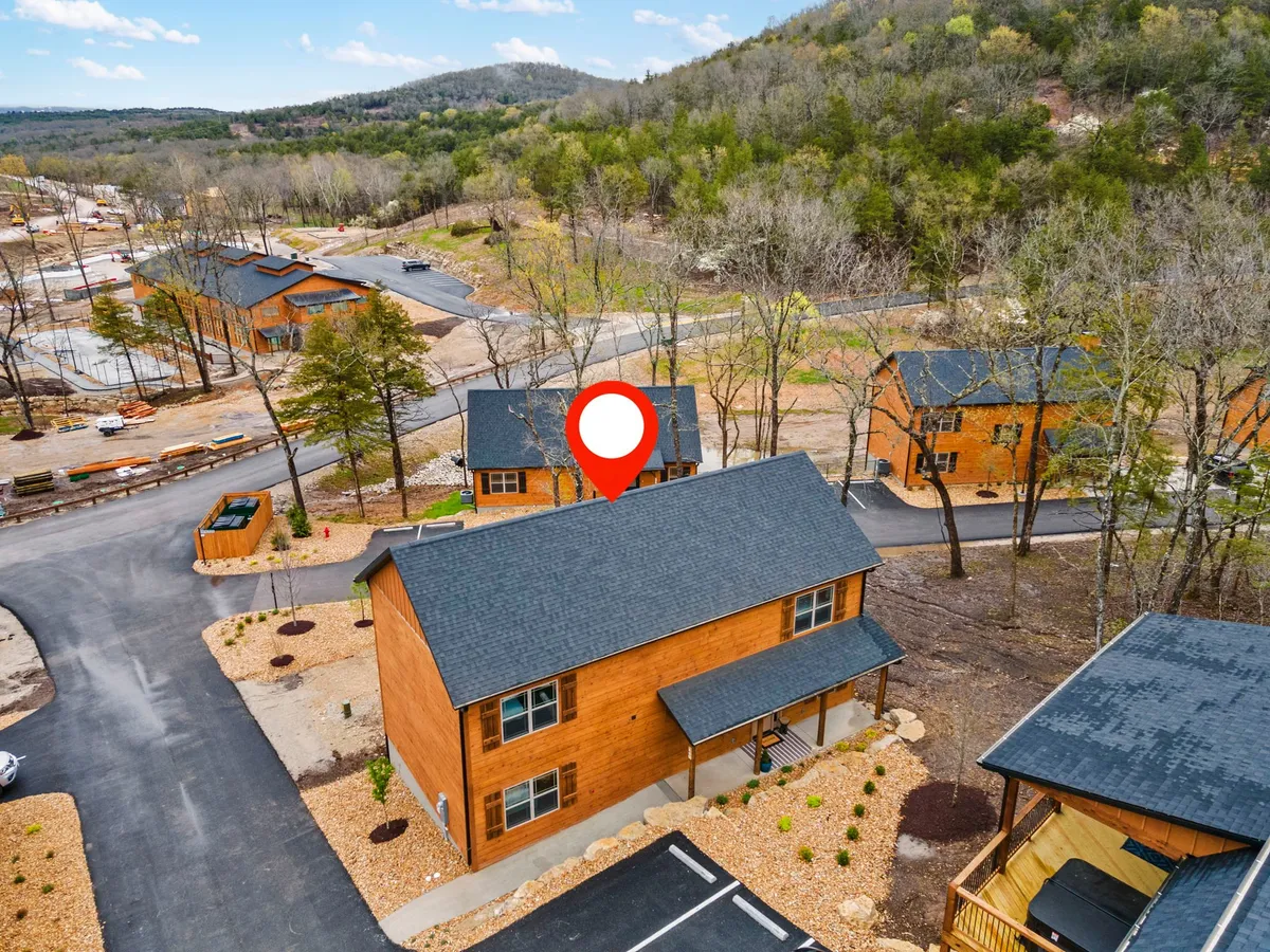 A relaxing view of the wooden cabin set amidst surrounding nature, with visible pathways and a parking area. The scene suggests direct access to outdoor activities, with plenty of green space for walks, hikes, and adventure.