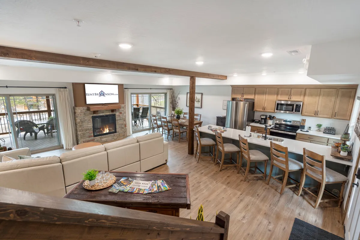 This image features an inviting open-concept interior that seamlessly connects the living room, kitchen island, dining area, and a comfortable sofa. The soft glow from the fireplace adds warmth, while the spacious layout encourages group gatherings and interaction.