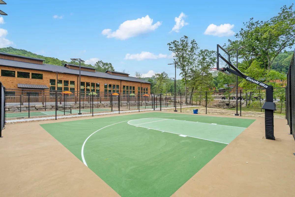 An outdoor basketball court set against a backdrop of trees and a modern building. The court is ready for friendly competitions or group games, with plenty of space for active fun amidst nature.