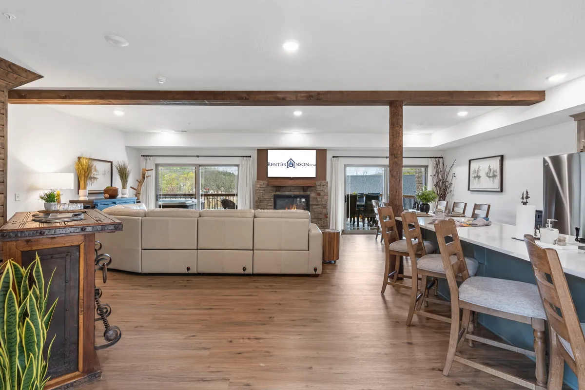 The photo highlights a cozy living area with a large sectional sofa, kitchen island with bar stools, a glowing fireplace, and a television. The arrangement naturally brings people together for conversation, entertainment, and relaxation.